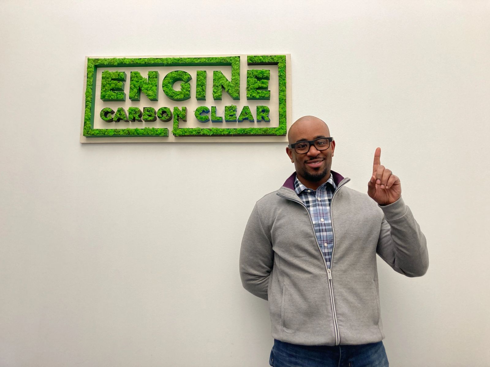 Team member standing beside the living-moss Engine Carbon Clear sign in the Montreal office